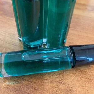 May include: A collection of small, clear glass bottles filled with a vibrant teal liquid. The bottles have black caps. One bottle lies horizontally, displaying the liquid. The background is a wooden surface.