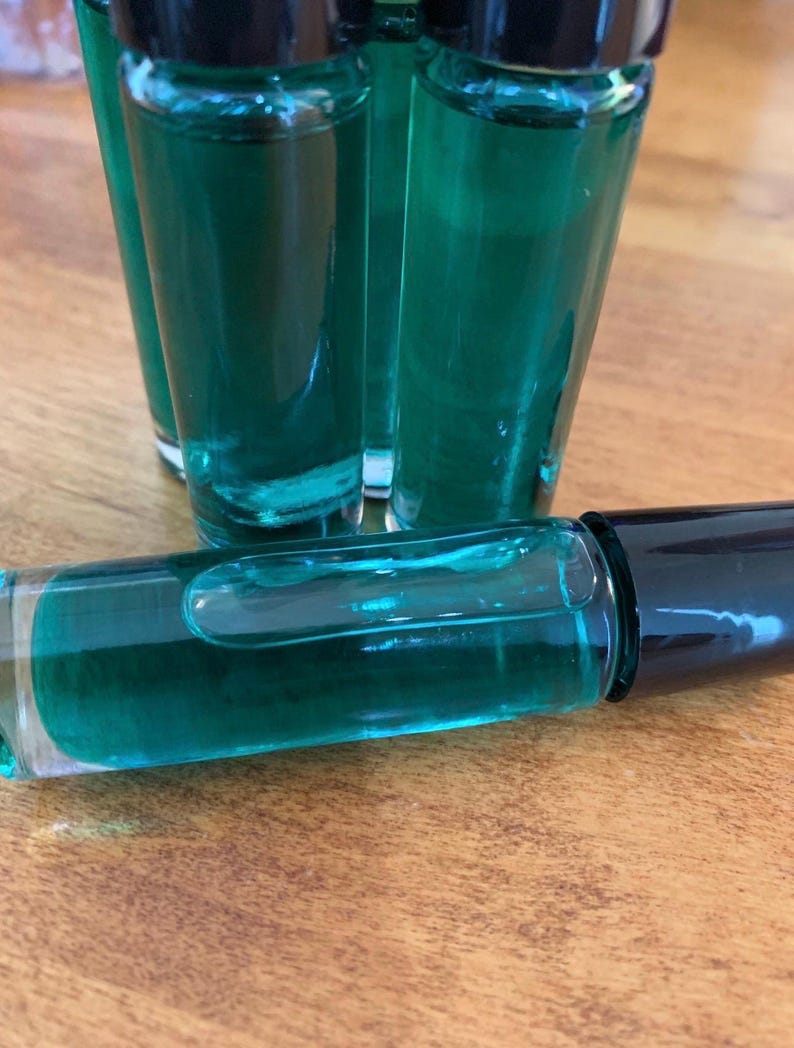 May include: A collection of small, clear glass bottles filled with a vibrant teal liquid. The bottles have black caps. One bottle lies horizontally, displaying the liquid. The background is a wooden surface.