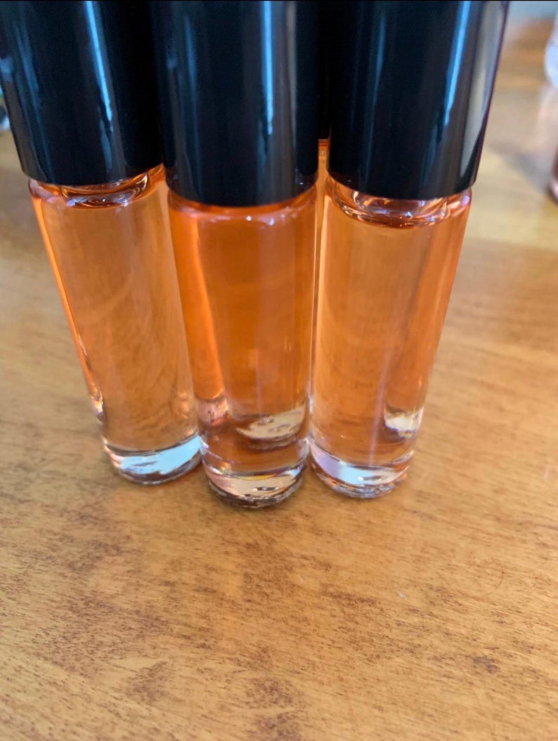 May include: Three clear glass roll-on bottles filled with orange liquid, with black caps. The bottles are arranged on a wooden surface. The bottles are partially in focus, with the liquid inside appearing bright. The bottles are approximately 10 cm tall.