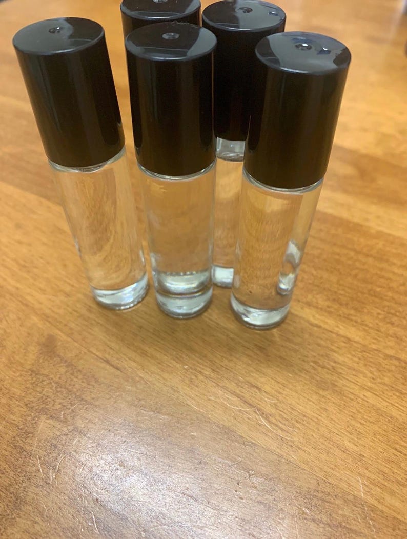May include: Five clear glass roll-on bottles with black caps. The bottles are filled with a clear liquid and are arranged on a wooden surface. The caps are cylindrical and opaque, contrasting with the transparent bottles.