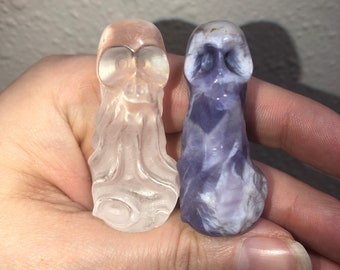 May include: Two small, hand-carved crystal skull figurines. One is clear and the other is purple and white.