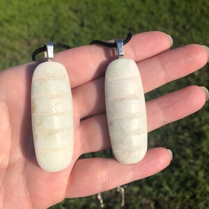 May include: Two white stone pendants with a ribbed texture and silver bail. The pendants are hanging from black cords.