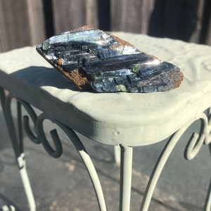 May include: A black and green mineral specimen with a rough, irregular shape. The mineral has a metallic sheen and is composed of many small, flat crystals.