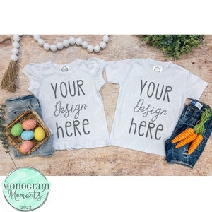 May include: Two white t-shirts with the text "Your Design Here" on a wooden background with Easter decorations.