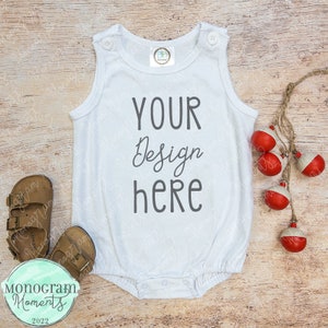 May include: White sleeveless baby onesie with the text "YOUR Design here" on a wood background.