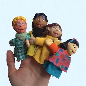 May include: Four finger puppets featuring diverse characters. One has blonde hair and glasses in a green plaid shirt, one has dark hair in a yellow coat, one has brown hair in a yellow top, and one has black hair in a pink patterned vest over blue.