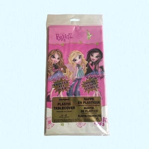 May include: A rectangular plastic tablecover in a pink and white color scheme, featuring Bratz character graphics and the text "PRINTED ALL OVER!" and "PLASTIC TABLECOVER 54" x 84" 137cm x 213cm". The packaging includes branding and product details.