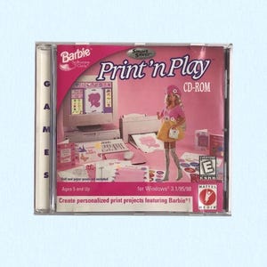 May include: A Barbie Print 'n Play CD-ROM software case for Windows 3.1/95/98. The pink cover features a computer, printer, and a Barbie doll illustration. Text includes 'Barbie', 'Print 'n Play', 'CD-ROM', 'Ages 5 and Up', and 'Mattel Media'.