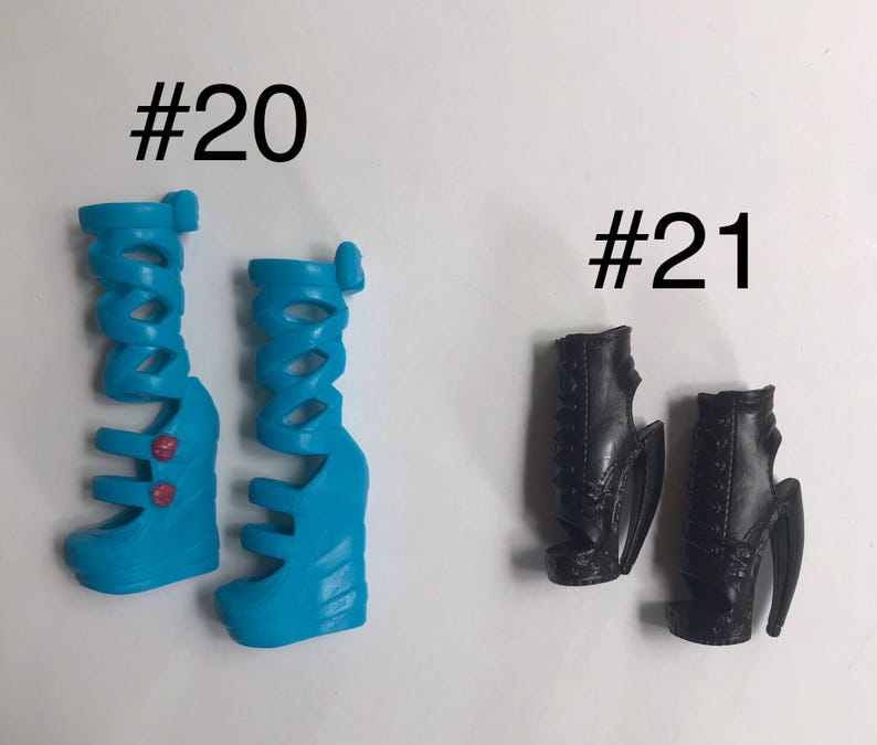 May include: Two pairs of doll shoes labeled #20 and #21. Pair #20 consists of bright blue, knee-high gladiator-style wedge sandals with two small red circular accents. Pair #21 features black, ankle-high open-toe wedge boots with lace-up detailing.
