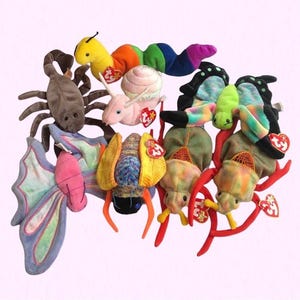 May include: A collection of nine colorful plush toys shaped like various insects, including a butterfly, a ladybug, a snail, a scorpion, and a caterpillar. The toys are all made by Ty and have the signature Beanie Baby tag.