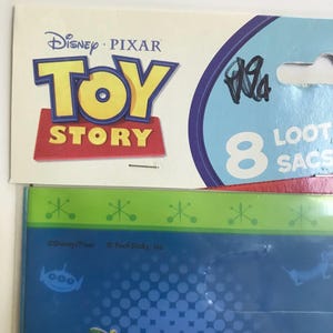 Puede incluir: Un paquete de la marca Disney Pixar Toy Story que contiene 8 bolsas de regalo. El empaque presenta el logotipo de Toy Story en amarillo y rojo sobre un fondo crema, con detalles y texto en azul. Debajo, un panel azul y verde muestra el logo.
