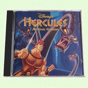May include: A Disney's Hercules Action Game CD-ROM in a clear plastic case. The cover art shows Hercules with a sword, facing menacing creatures, with the game title in gold on a blue background.