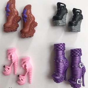 May include: Four pairs of doll shoes labeled #13, #14, #15, and #16. Pair #13 is brown with purple bows. Pair #14 is black with gray brick-patterned platforms. Pair #15 is light pink with spiral heels. Pair #16 is purple with studs and silver buckles.