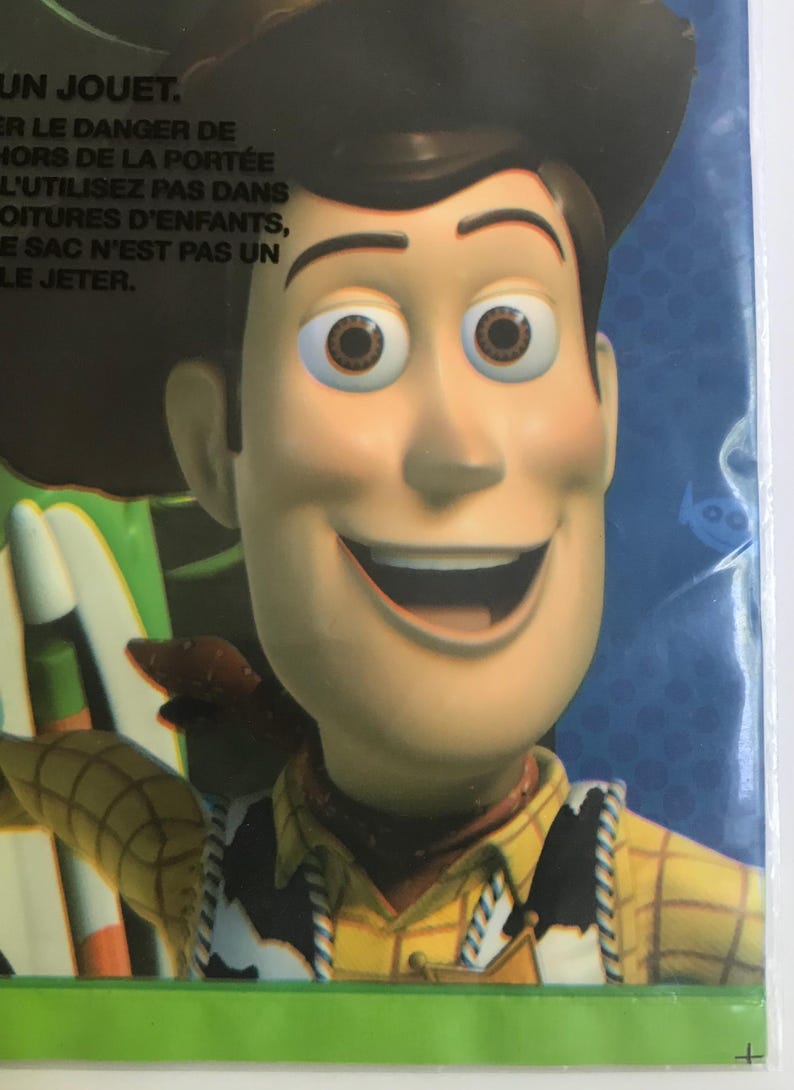 Puede incluir: Un empaque de pl&aacute;stico que presenta un primer plano del personaje Woody de Toy Story, con un sombrero de vaquero marr&oacute;n, una camisa de cuadros amarillos con un chaleco de estampado de vaca en blanco y negro y una insignia de sheriff dorada.