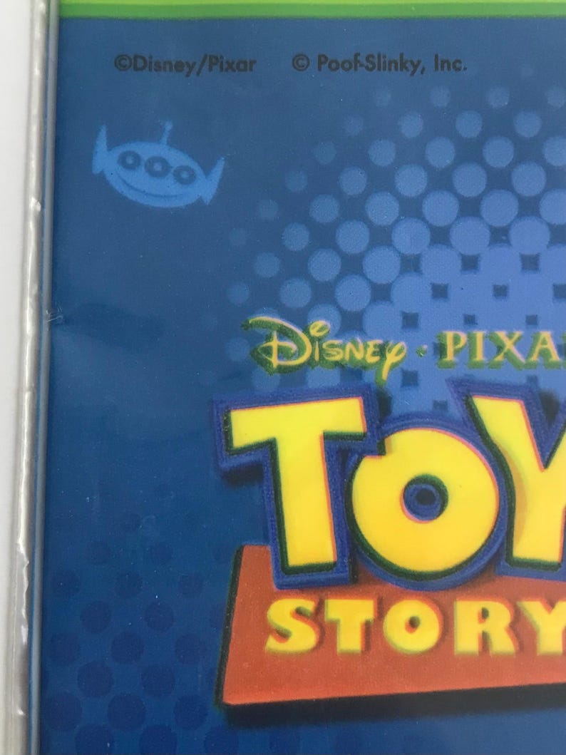 Puede incluir: Un empaque de producto azul que presenta el logotipo de Toy Story en letras amarillas y rojas. El dise&ntilde;o incluye un peque&ntilde;o gr&aacute;fico de un alien&iacute;gena azul y el texto Disney/Pixar y Poof-Slinky, Inc. impreso en la parte superior sobre un fondo azul con puntos.