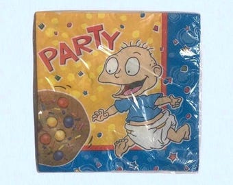 May include: A package of party napkins featuring a cartoon character and the word "PARTY" in red. The napkins have a yellow background with confetti and a blue border with stars and shapes. A cookie with colorful candies is also visible.