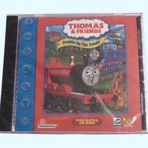 May include: A Thomas & Friends "Trouble On The Tracks" CD-ROM game in a clear plastic case. The cover features a red train, Thomas, and other characters. The case has a blue spine with buttons. The game is an interactive CD-ROM.