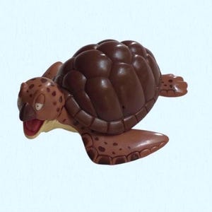 May include: A brown turtle figurine with a detailed shell and flippers. The turtle's head is tan with brown spots and an open red mouth. The figurine is a cartoon-like design.