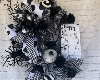 May include: Black and white Halloween wreath with a sign that says "happy halloween". The wreath is made with mesh, ribbon, and other decorative elements.