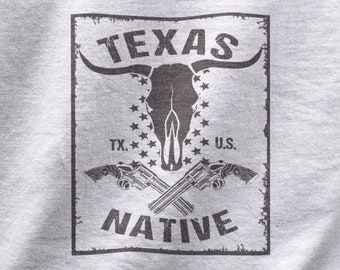May include: A distressed, black and white graphic design with the text "TEXAS NATIVE" in a vintage style. The graphic features a bull skull with horns, two crossed pistols, and the text "TX." and "U.S."