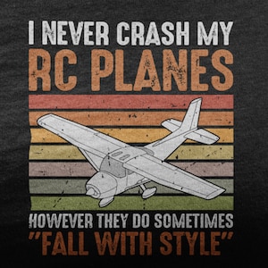 May include: A black t-shirt with a vintage-style graphic that says "I never crash my RC planes, however they do sometimes "fall with style"". The graphic features a white silhouette of a small airplane against a colorful striped background.