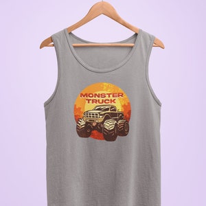 Puede incluir: Una camiseta sin mangas gris con un gr&aacute;fico de un cami&oacute;n monstruo en una puesta de sol. El texto "Monster Truck" est&aacute; impreso en rojo sobre el cami&oacute;n.