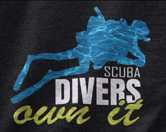 Puede incluir: Una camiseta negra con una silueta azul de un buceador con el texto "SCUBA DIVERS own it" en blanco y amarillo.