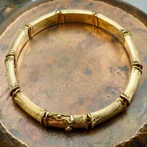 May include: A gold bamboo-style bangle bracelet with a detailed clasp.