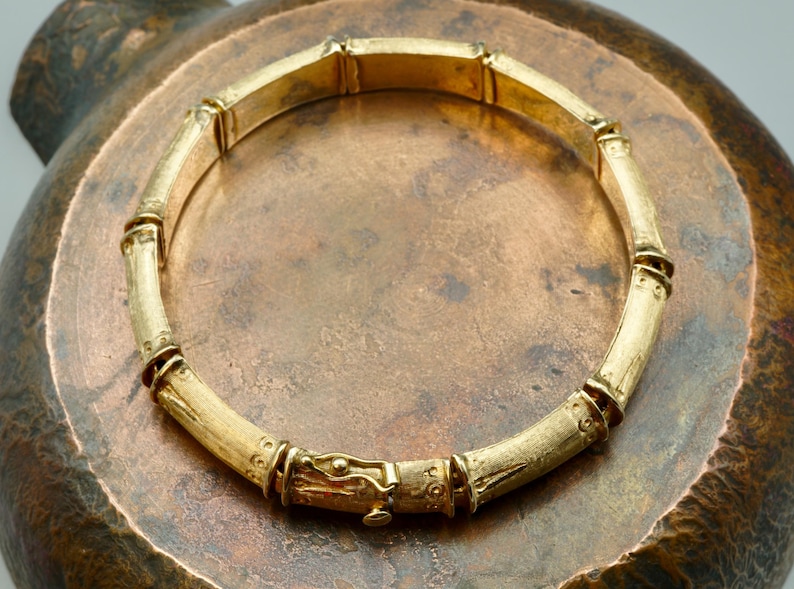 May include: A gold bamboo-style bangle bracelet with a detailed clasp.