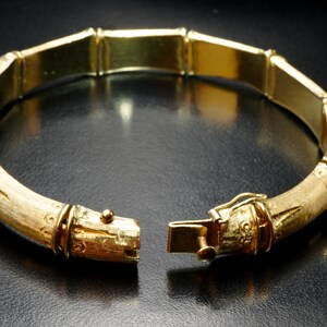 May include: A gold bamboo-style bangle bracelet with a hinged clasp. The bracelet is made of polished gold and has a textured finish.