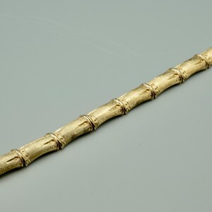 May include: A gold bamboo-style bracelet. The bracelet is made of linked sections that resemble bamboo stalks.