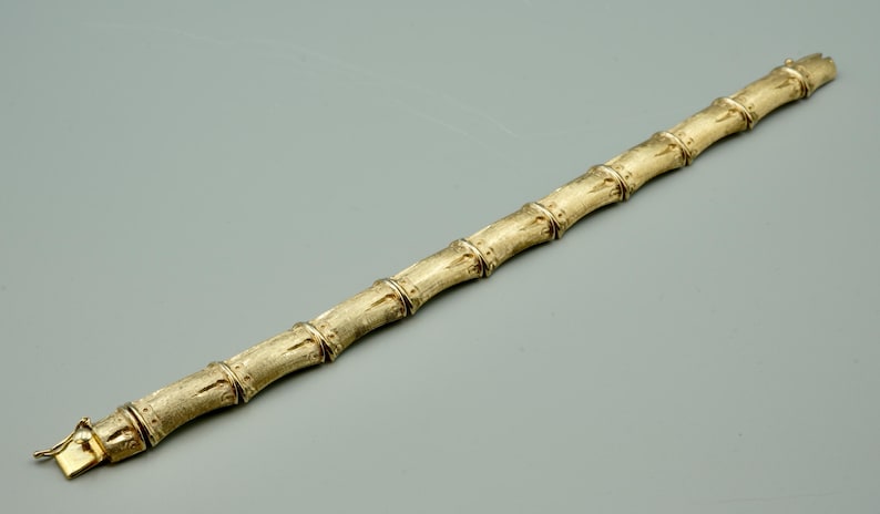 May include: A gold bamboo-style bracelet. The bracelet is made of linked sections that resemble bamboo stalks.