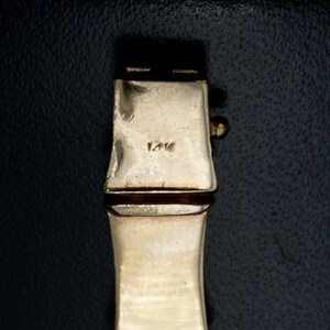 May include: Close-up of a gold-toned metal bracelet clasp with the inscription "14K" on the back.