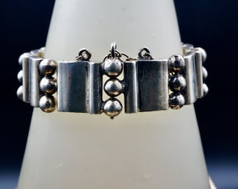May include: A silver bracelet with a geometric design. The bracelet is made up of rectangular and round shapes. The clasp is a simple hook and eye.