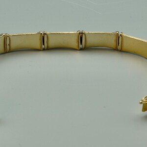 May include: A gold-toned bangle bracelet with a bamboo-inspired design. The bracelet is made of multiple linked sections, each with a slightly curved shape.