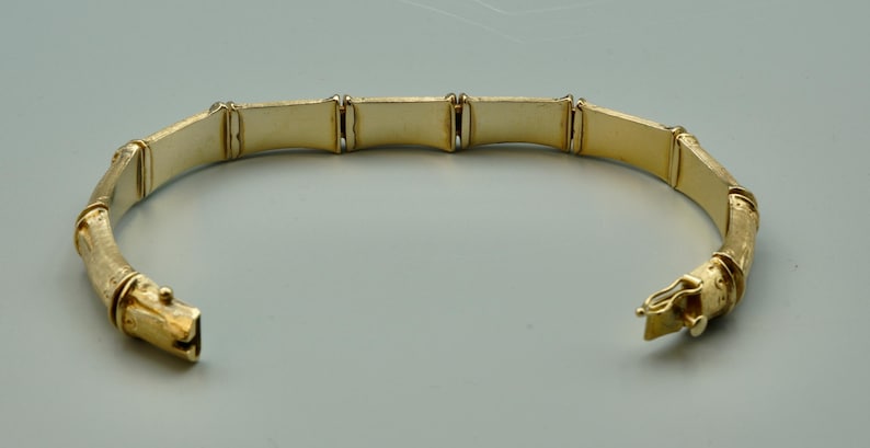 May include: A gold-toned bangle bracelet with a bamboo-inspired design. The bracelet is made of multiple linked sections, each with a slightly curved shape.