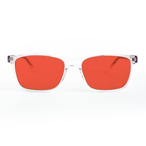 May include: Transparent-framed sunglasses with vivid orange lenses. The rectangular frames have a clear appearance, and the lenses are a solid, bright orange. The temples have small, square details. The sunglasses are set against a white background.