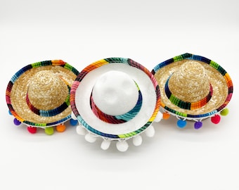 May include: Three colorful Mexican sombreros with white felt tops and colorful trim. Each sombrero has a white pom-pom trim around the brim.