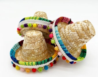 May include: Three miniature straw sombreros with colorful trim and pom-poms. The sombreros are stacked on top of each other.