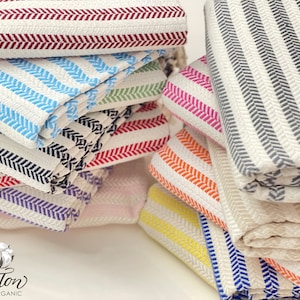 May include: A stack of colorful striped towels made of 100% organic cotton. The towels are folded and arranged in a pyramid shape. The towels are in various colors, including red, blue, pink, orange, yellow, and white.