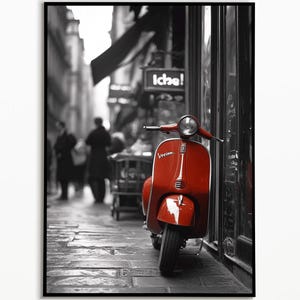 May include: A red Vespa scooter parked on a cobblestone street in a black and white city setting. The scooter is parked next to a building with a sign that reads "Iche!" in black and white.