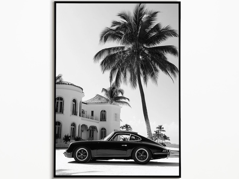 May include: A black and white photograph of a black Porsche 911 parked in front of a white house with palm trees in the background.