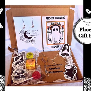 May include: A brown cardboard gift box filled with various items, including a necklace with a ghost charm, bath bombs, stickers, a lollipop, and two cards. One card features a ghost with the text "Phoebe Fucking Bridgers" and the other card features a moon and stars with the text "If I could give you the moon, I would give you the moon".