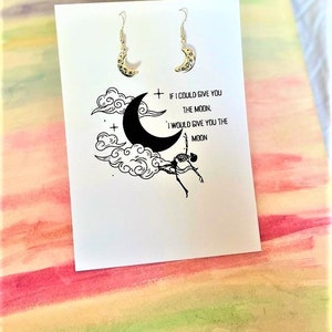 May include: A pair of silver crescent moon earrings with a delicate design. The earrings are displayed on a white card with the text "If I could give you the moon, I would give you the moon."