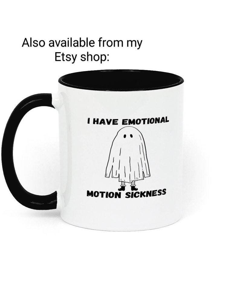 May include: White coffee mug with a black rim and handle. The mug has a black and white illustration of a ghost with the text "I have emotional motion sickness".