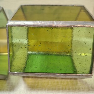 May include: A square-shaped glass box constructed with translucent lime green and yellow panels joined by silver-toned metal solder lines. The glass features visible air bubbles throughout the surface, creating a textured appearance within the frame.