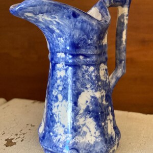 May include: A small, blue and white ceramic pitcher with a handle and spout. The pitcher has a marbled design with shades of blue and white. The handle is curved, and the spout is pointed. The pitcher is likely used for serving liquids.