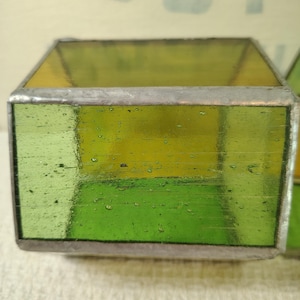 May include: A rectangular glass block featuring translucent lime green panels joined by silver-toned metal solder lines. The glass has a visible texture with small air bubbles throughout, creating a semi-transparent appearance with a smooth finish.