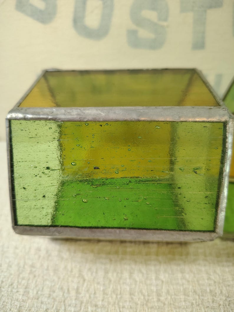 May include: A rectangular glass block featuring translucent lime green panels joined by silver-toned metal solder lines. The glass has a visible texture with small air bubbles throughout, creating a semi-transparent appearance with a smooth finish.