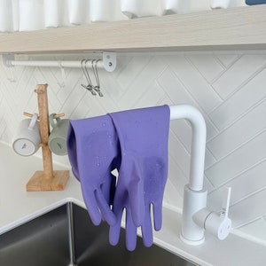 May include: A white kitchen faucet with a purple pair of dishwashing gloves hanging from the spout. The faucet has a lever handle and a white, rectangular soap dispenser.